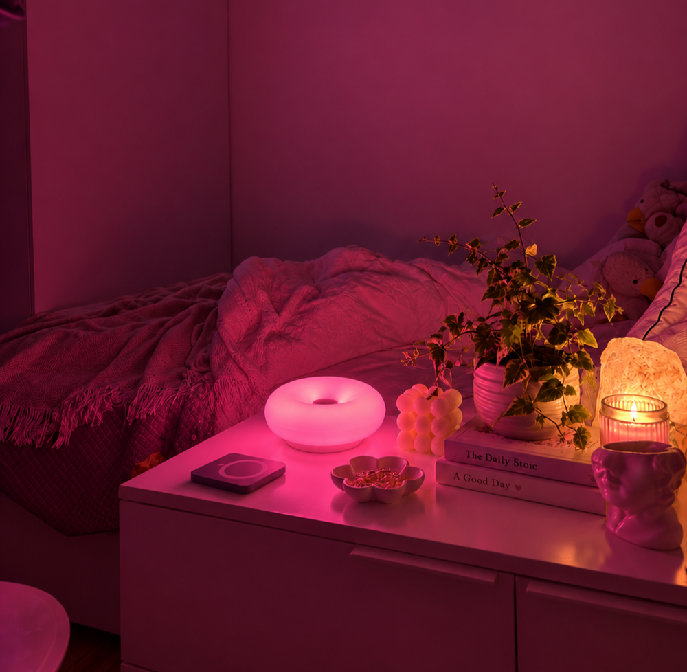 Pink glowing disc-shaped lamp on a bedside table