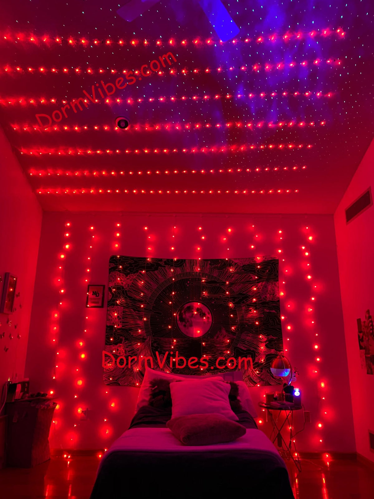 Red ceiling light strands above a narrow bed and moon tapestry