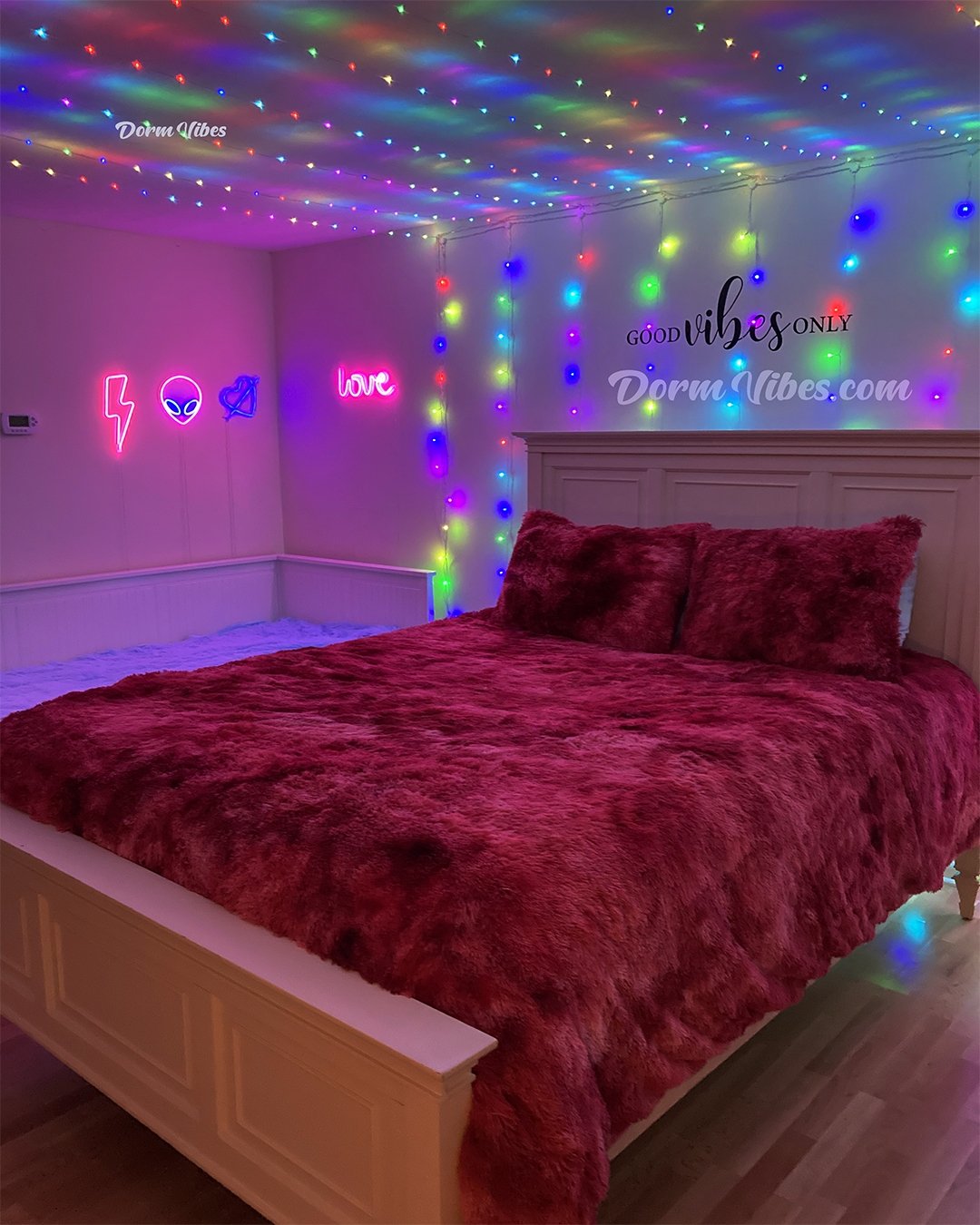 Rainbow ceiling lights above a bed with deep red fluffy bedding