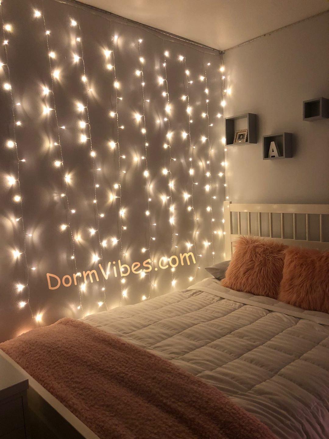 Warm white curtain lights hanging behind a bed with peach pillows