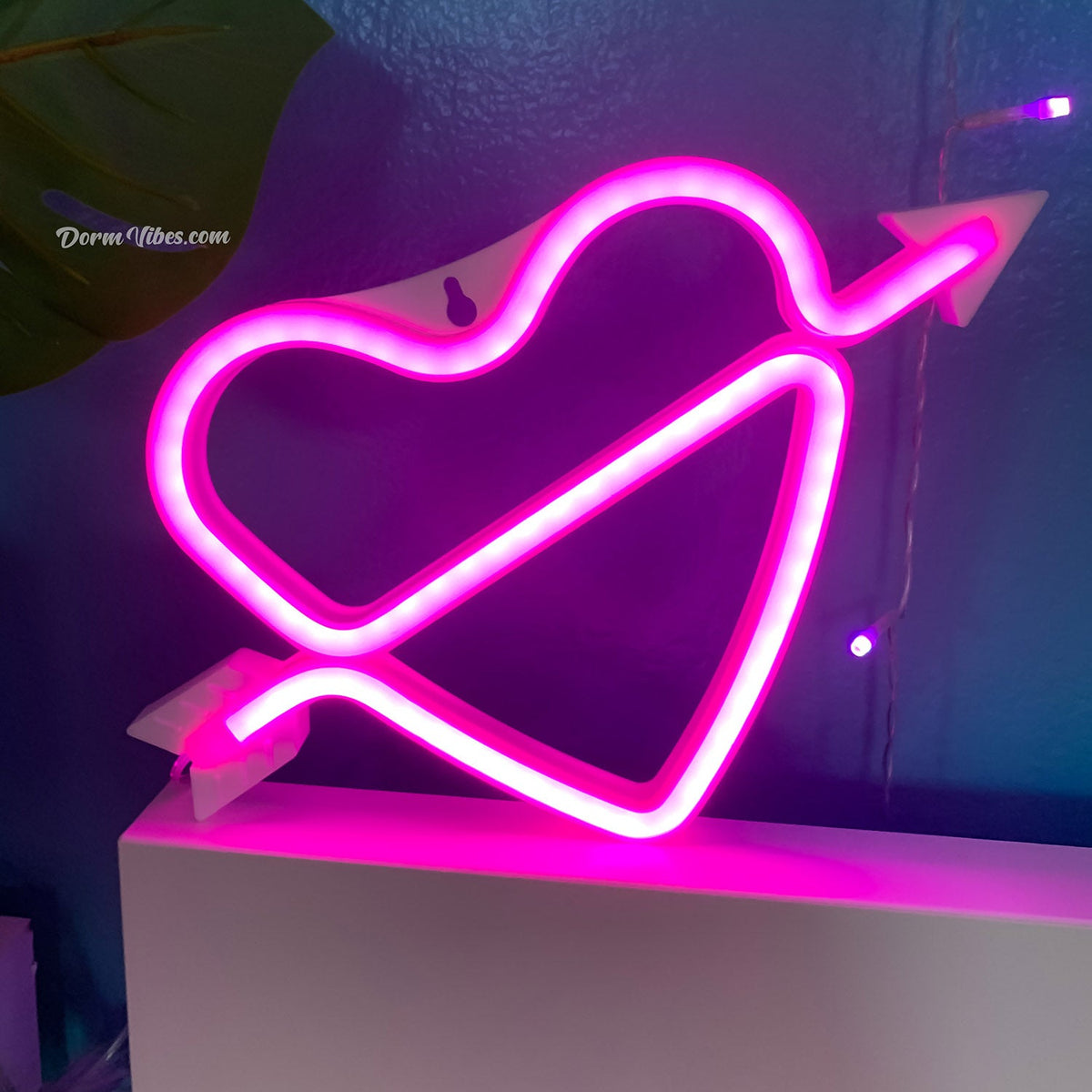 Pink heart-and-arrow neon sign on top of a white cabinet