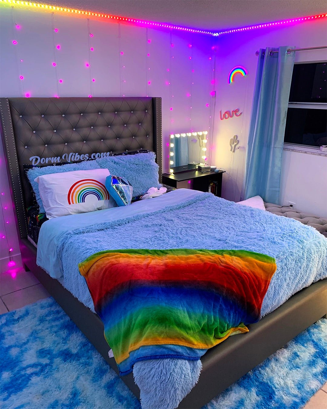 Rainbow neon sign above a blue bed with a rainbow throw